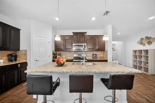 a kitchen with stainless steel appliances granite countertop a stove top oven a sink a dining table and chairs with wooden floor