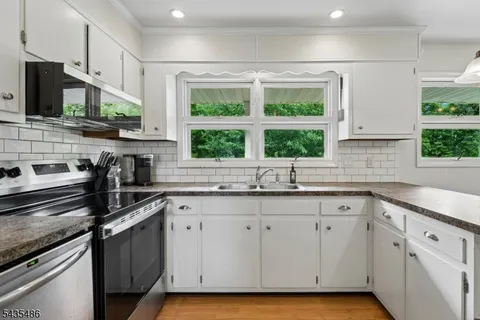 a kitchen with granite countertop white cabinets white appliances a sink and a window