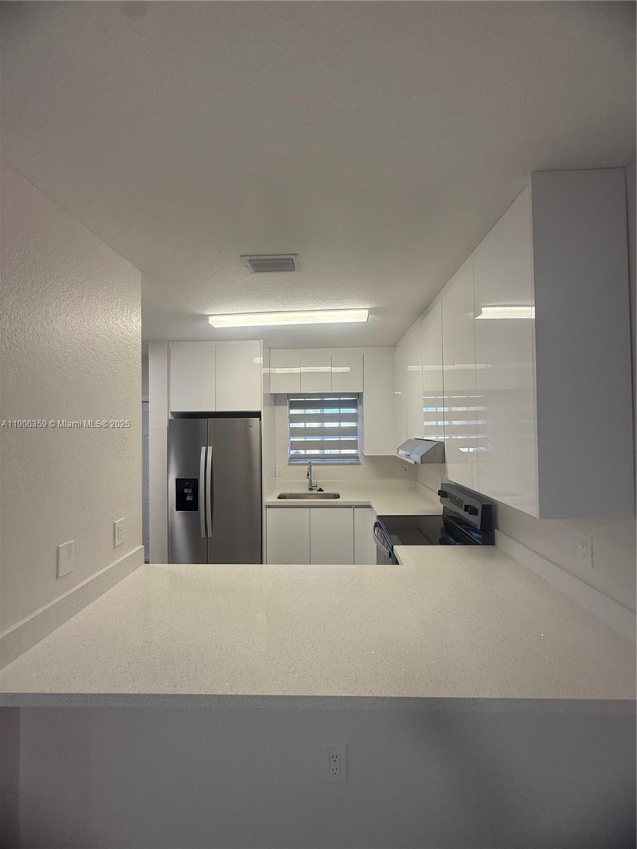 6752 Northwest 182nd Street, Unit 101 Hialeah, FL 33015 - Photo 5 of 23 a large white kitchen with a sink and dishwasher a stove top oven with wooden floor