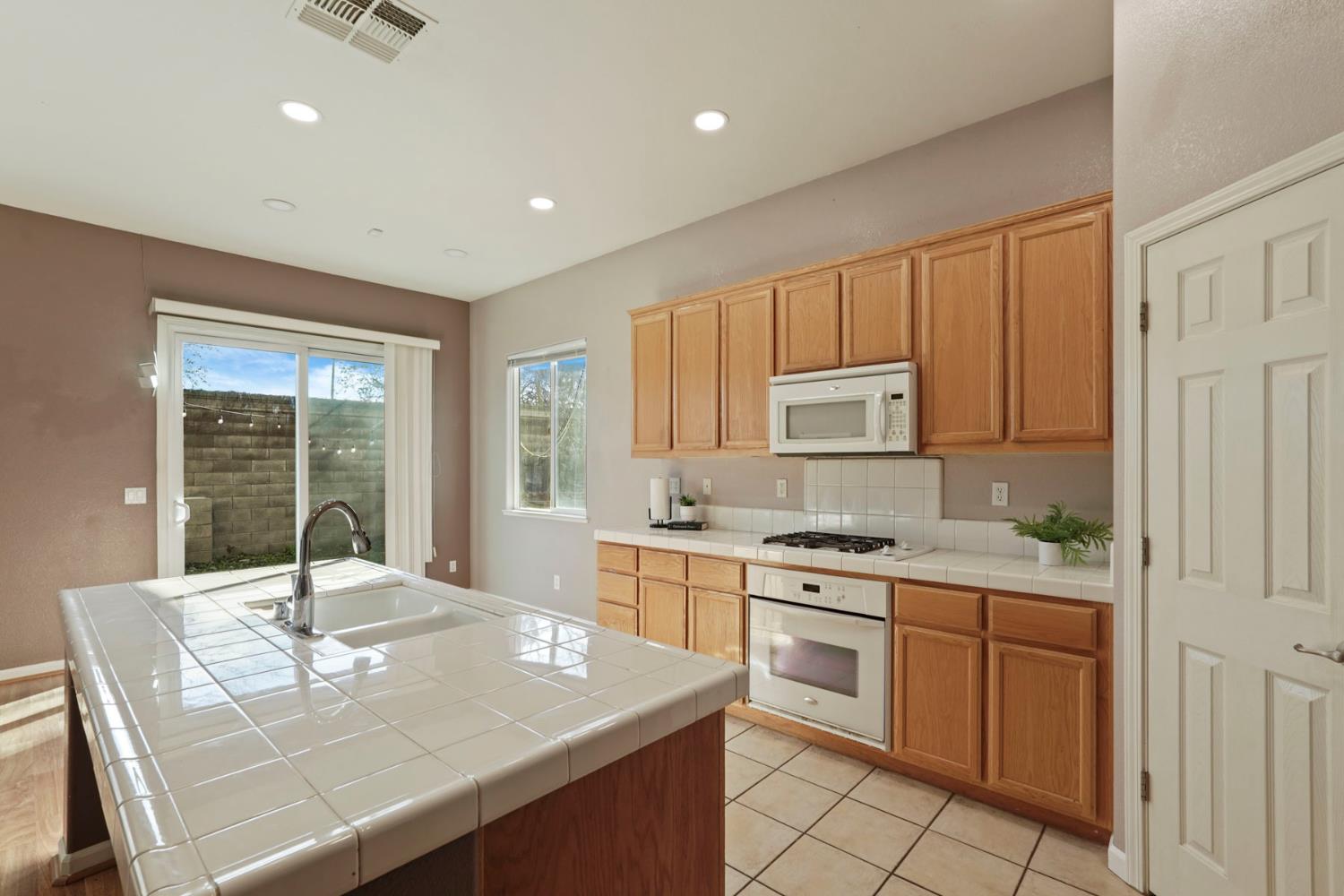 904 Sebastian Lane Manteca, CA 95336 - Photo 9 of 21 a kitchen with kitchen island granite countertop a stove a sink and white cabinets with wooden floors