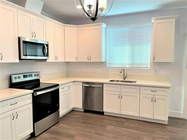a kitchen with stainless steel appliances granite countertop white cabinets a sink a stove a microwave and wooden floors