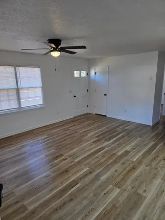 an empty room with wooden floor fan and windows