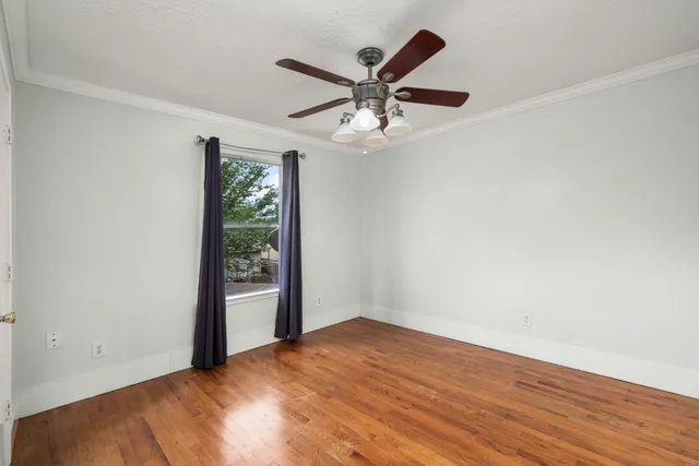 an empty room with wooden floor ceiling fan and windows