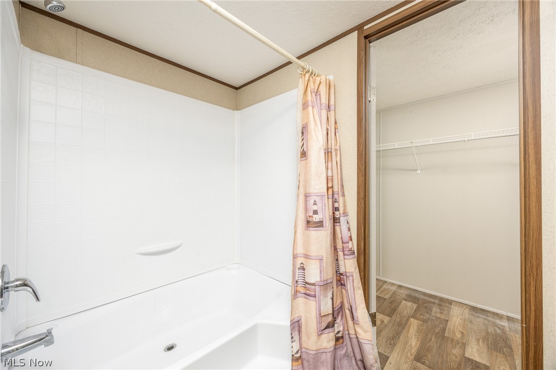 7455 Stanleyville Road Whipple, OH 45788 - Photo 18 of 37 Bathtub with white surround and chrome fixtures, featuring wood-finish flooring extending into a closet space with wire shelving