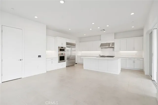a large white kitchen with stainless steel appliances cabinets a sink and a refrigerator