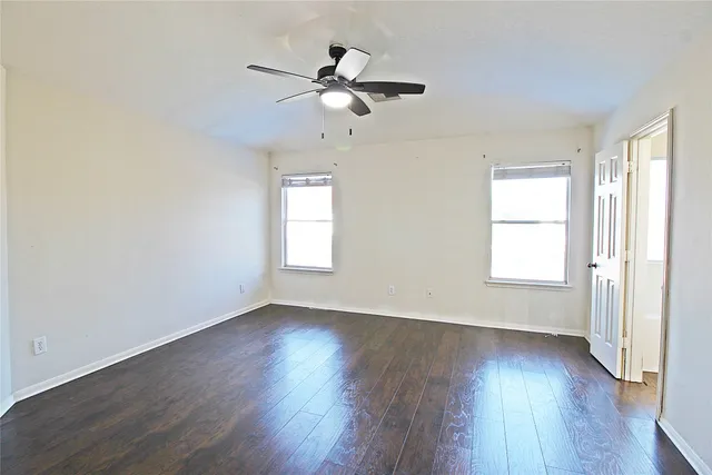 an empty room with wooden floor fan and windows