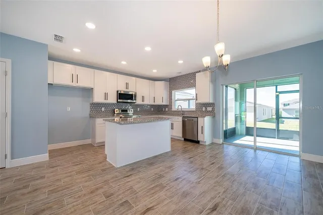 a kitchen with stainless steel appliances granite countertop a refrigerator a sink dishwasher a stove and white cabinets with wooden floor