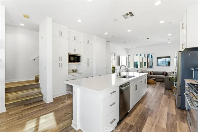 a large white kitchen with a stove a sink dishwasher and a refrigerator with wooden floor