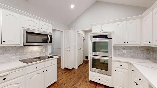 a kitchen with granite countertop white cabinets stainless steel appliances and wooden floor