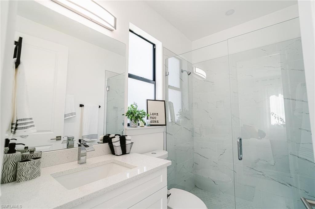907 Homestead Road South Lehigh Acres, FL 33974 - Photo 27 of 43 Contemporary bathroom featuring a spacious glass-enclosed shower with marbled wall tile, a white vanity with an integrated sink, a wide quartz countertop, and modern chrome fixtures