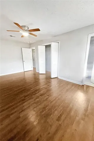 a view of an empty room with wooden floor and fan