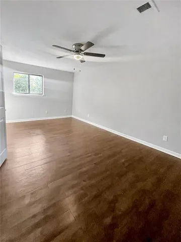 an empty room with wooden floor fan and windows