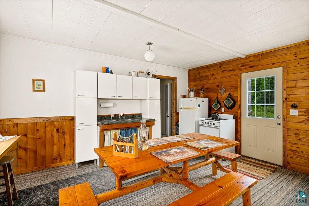 1268 Tom Lake Road Hovland, MN 55606 - Photo 5 of 56 Kitchen area featuring paneled wood walls and wainscoting, white upper cabinetry, a dual-basin sink with a dark countertop, and a white refrigerator and range