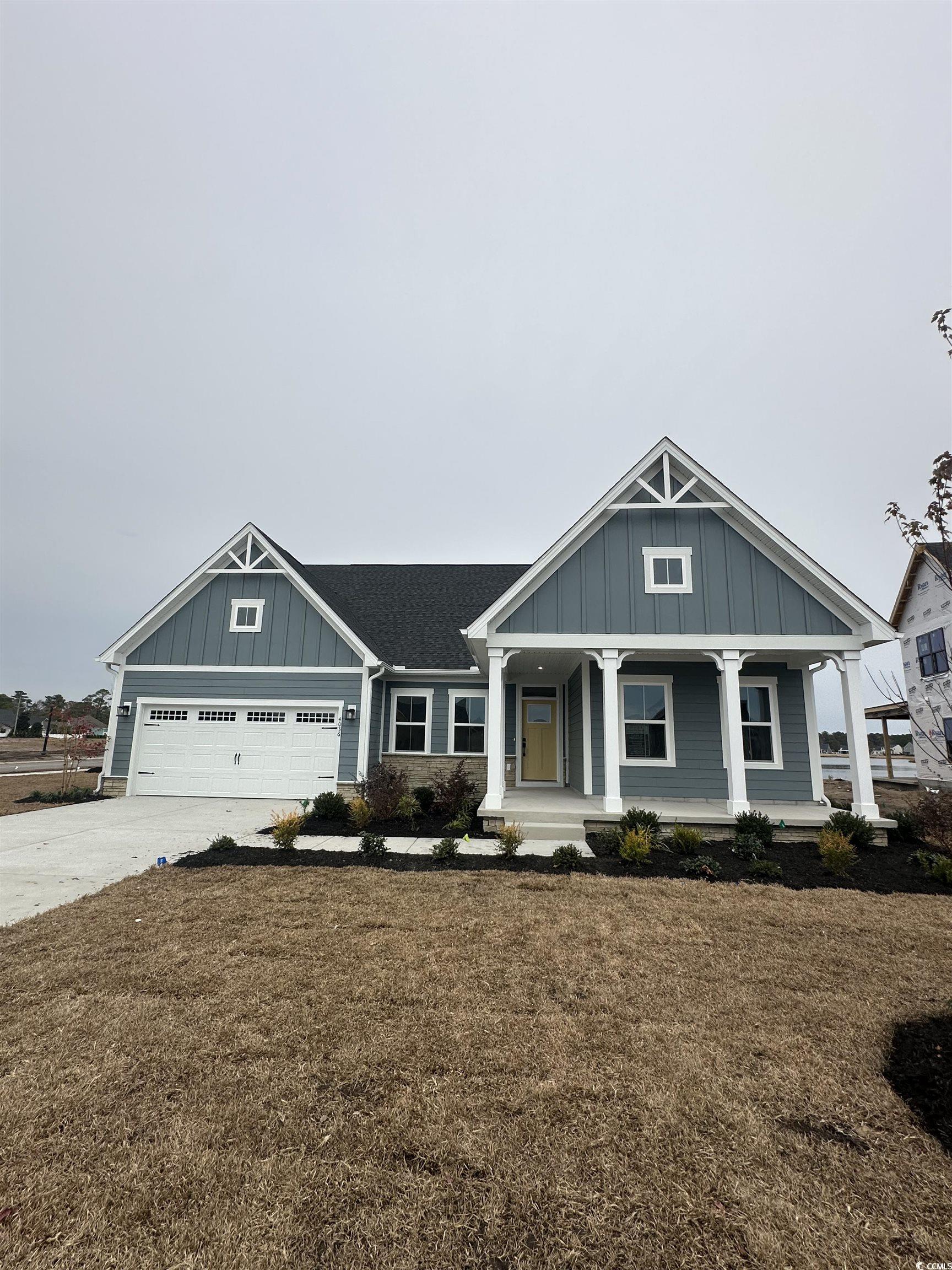 View of front of house with board and batten siding, covered porch, driveway, and a front lawn