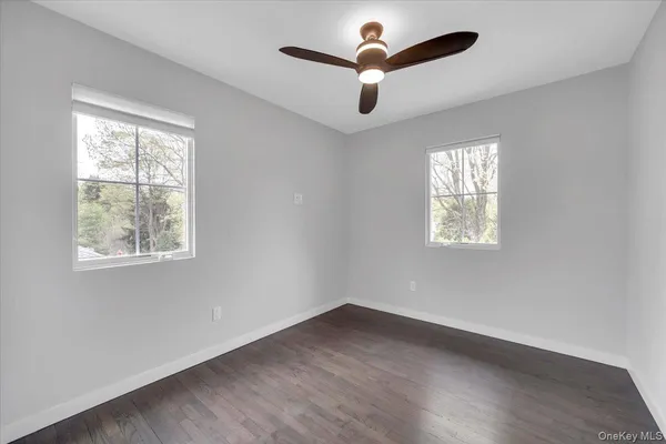 an empty room with wooden floor ceiling fan and windows