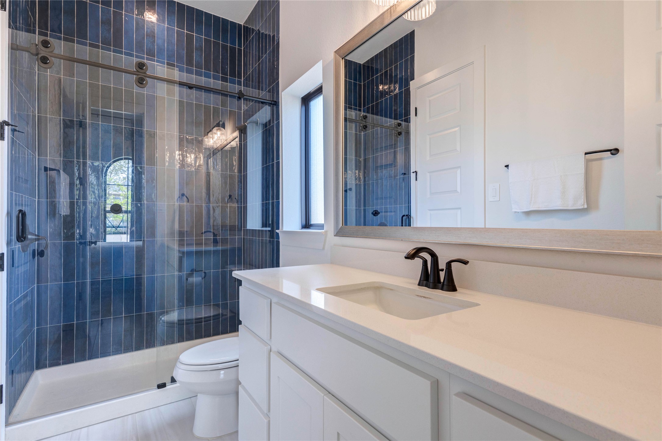 4510 Windmill Lndg Lane Fulshear, TX 77441 - Photo 24 of 48 This bathroom features a sleek, modern design with a double vanity in deep blue tile, black fixtures, and a large mirror. The space is bright with white walls and wood flooring, offering a clean, stylish look.
