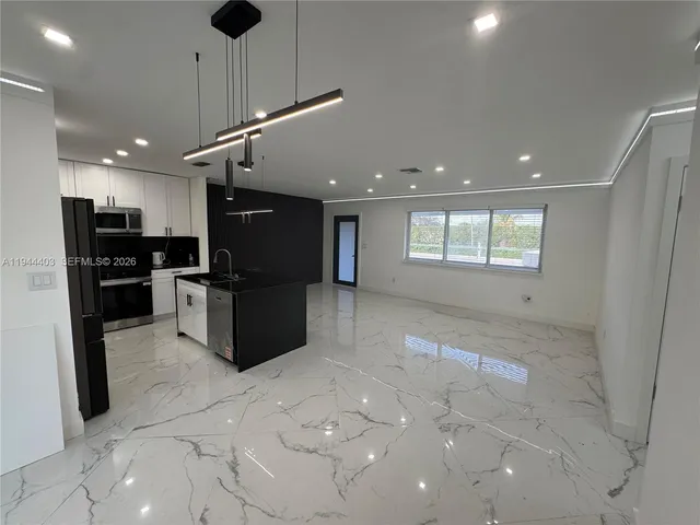 a large kitchen with stainless steel appliances kitchen island granite countertop a refrigerator and a stove top oven