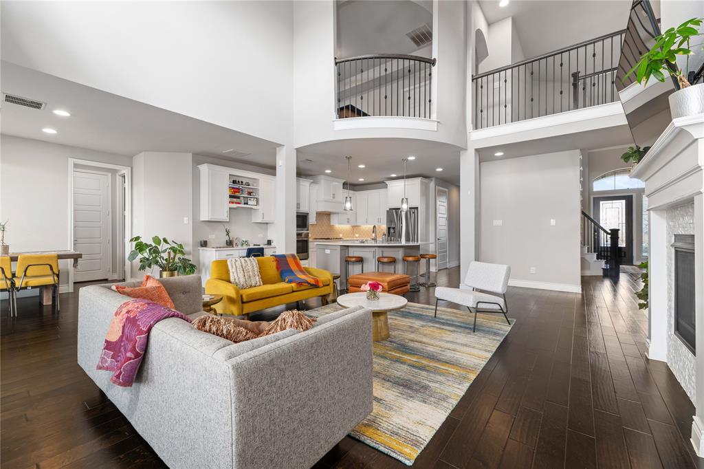 16541 Sweetgum Road Frisco, TX 75033 - Photo 22 of 26 Expansive living area with high ceilings, dark wood-finish flooring, a fireplace with a white mantel, and a multi-level layout featuring an open kitchen with white cabinetry