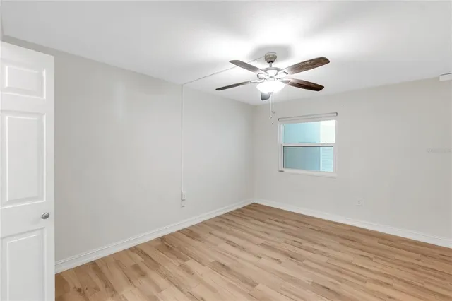 a view of an empty room with wooden floor and a ceiling fan