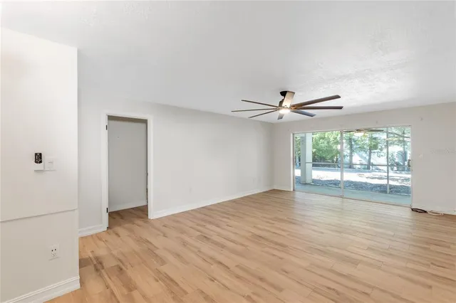 an empty room with wooden floor fan and windows