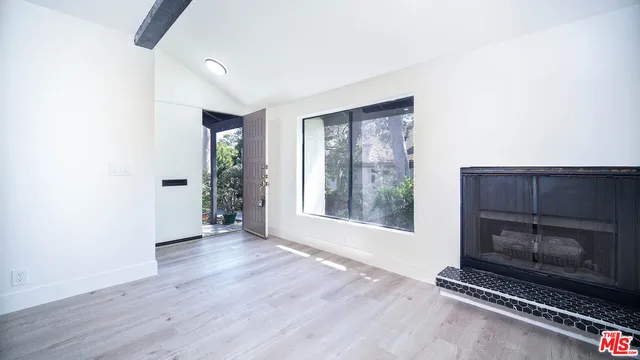 a view of an empty room with wooden floor fireplace and a window