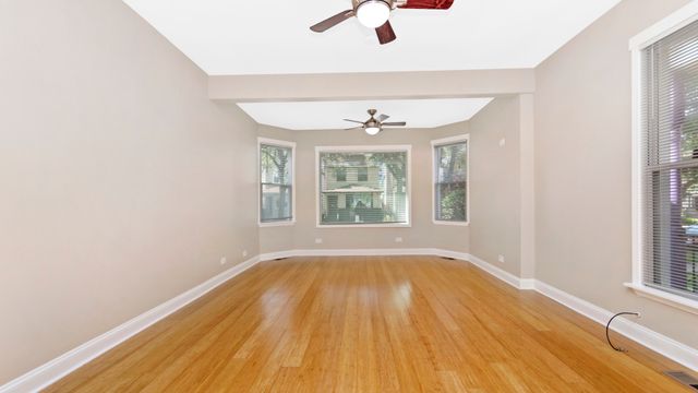 an empty room with wooden floor chandelier fan and windows