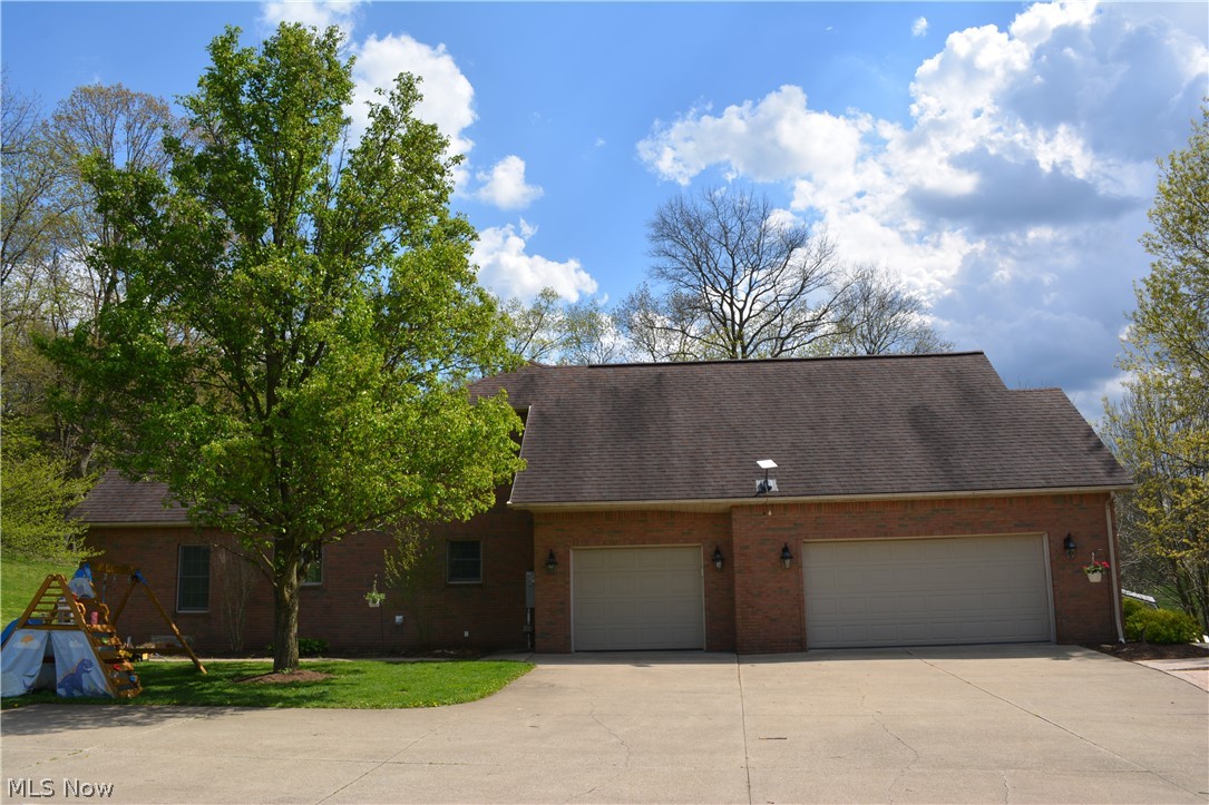 2363 Tabor Ridge Road Northeast New Philadelphia, OH 44663 - Photo 5 of 42 Brick exterior featuring a two-car garage with individual doors, a concrete driveway, and established landscaping including a mature tree