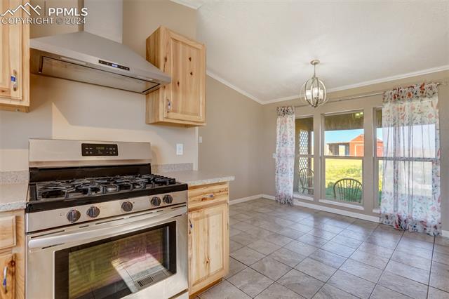 6240 Night Train Lane Yoder, CO 80864 - Photo 20 of 50 Kitchen featuring stainless steel gas range, an inviting chandelier, wall chimney exhaust hood, pendant lighting, and light tile floors