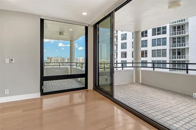 a view of an empty room with kitchen view and wooden floor