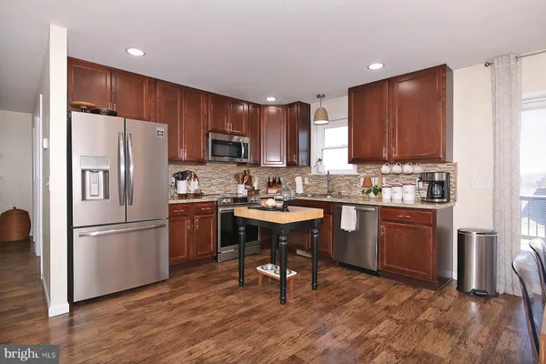 a kitchen with kitchen island granite countertop wooden floors appliances and cabinets