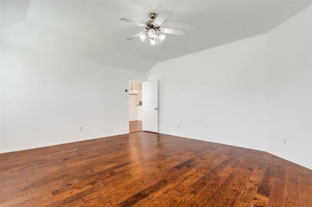 an empty room with wooden floor chandelier fan and windows