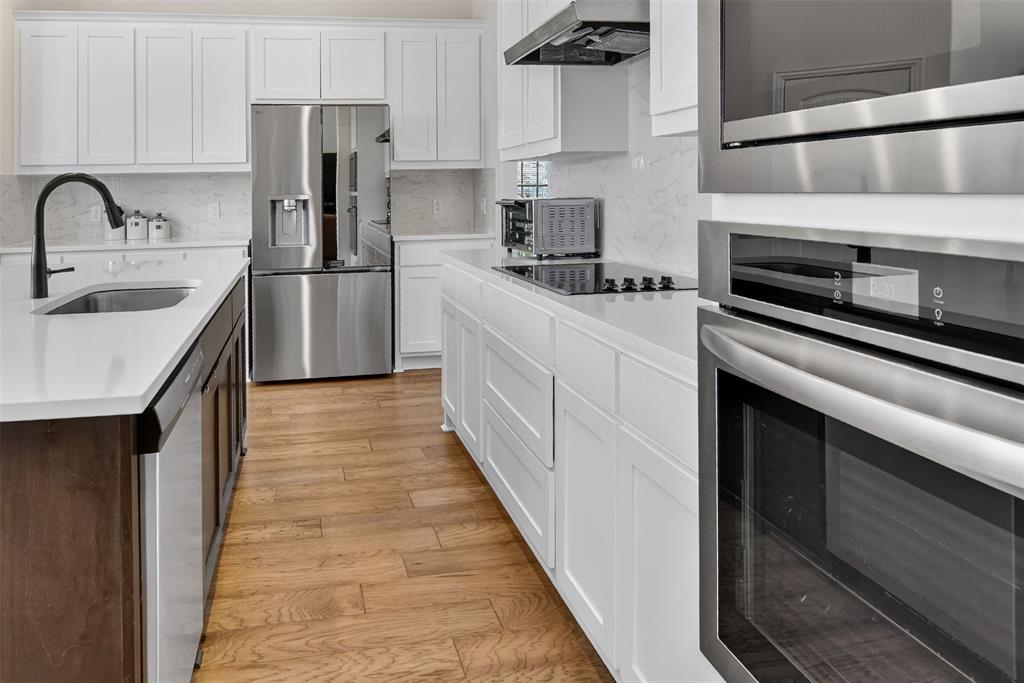 157 Misty Mountain Lane Rhome, TX 76078 - Photo 11 of 40 Kitchen with stainless steel appliances, two tone color scheme, light wood-style flooring, tasteful backsplash, and a center island with sink