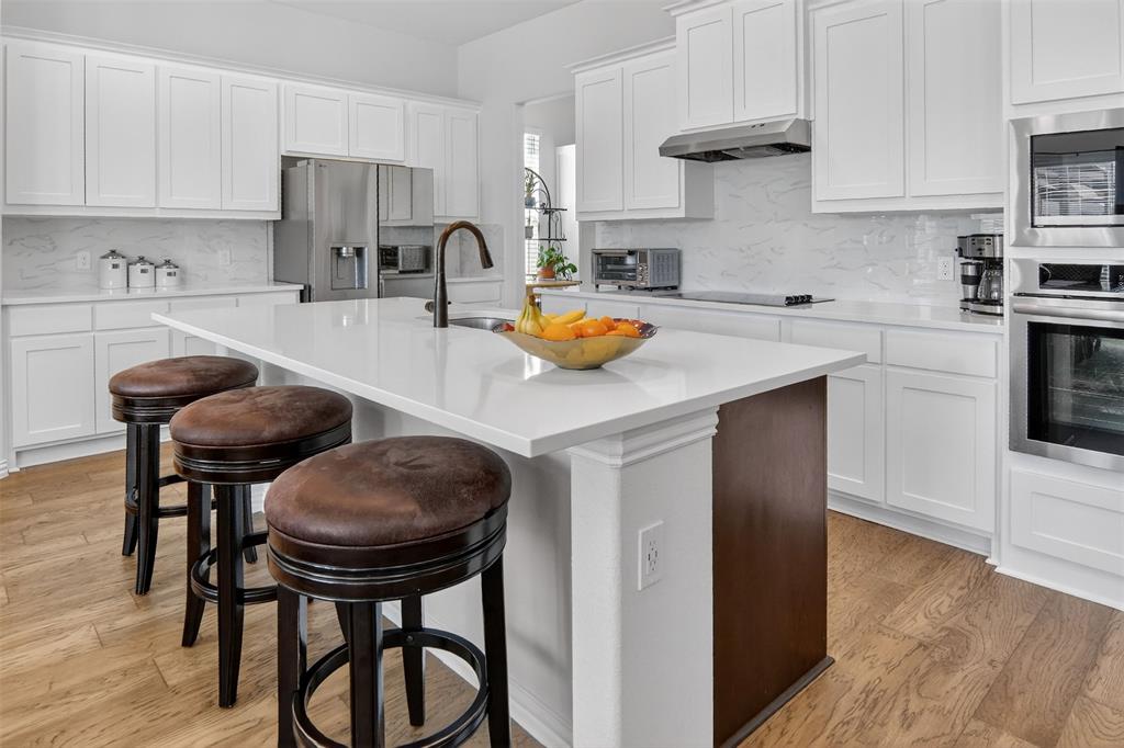 157 Misty Mountain Lane Rhome, TX 76078 - Photo 9 of 40 Kitchen featuring a breakfast bar area, light wood-type flooring, stainless steel appliances, white cabinets, and a kitchen island with sink