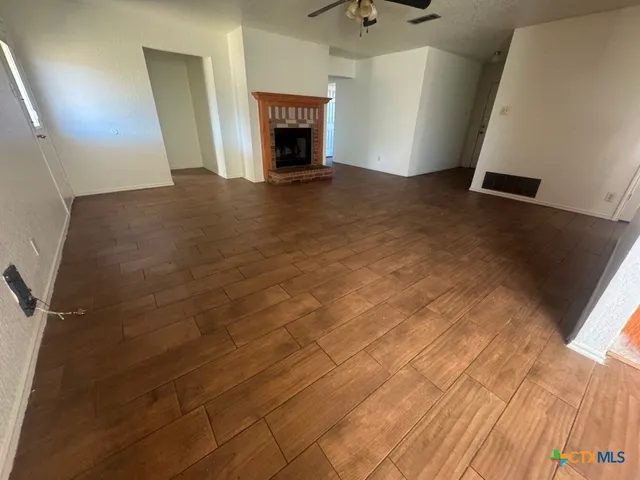 a view of an empty room with wooden floor fireplace and a window