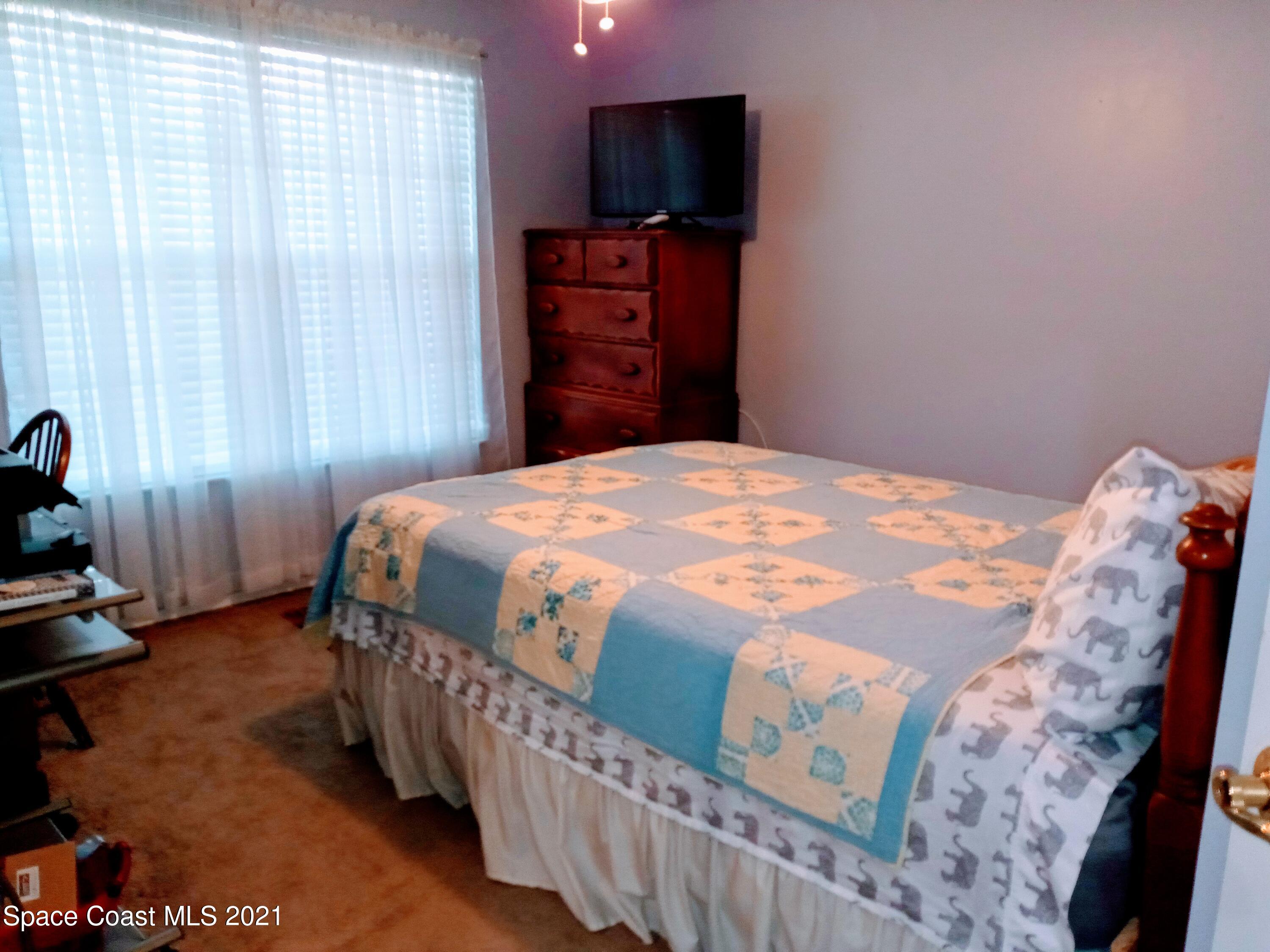 798 Riviera Drive Northeast Palm Bay, FL 32905 - Photo 3 of 7 a bedroom with a bed and a flat tv screen on a dresser