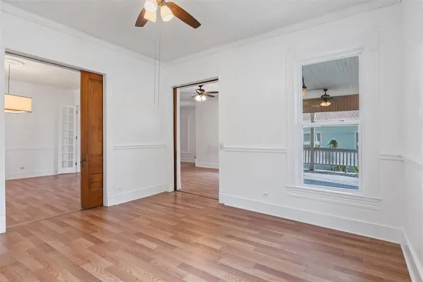an empty room with wooden floor chandelier fan and windows