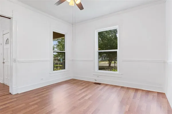 an empty room with wooden floor chandelier fan and windows