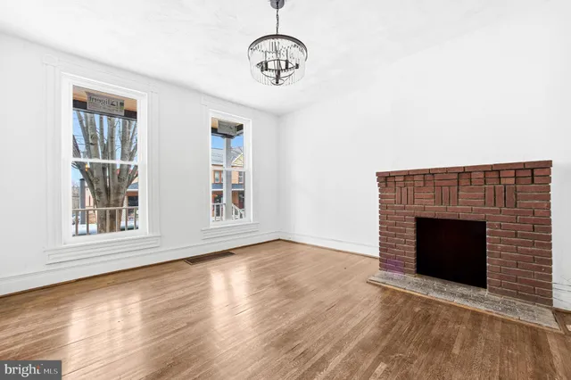 a view of an empty room with wooden floor fireplace and a window