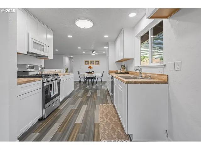 a kitchen with stainless steel appliances granite countertop a stove top oven a sink dishwasher and white cabinets with wooden floor