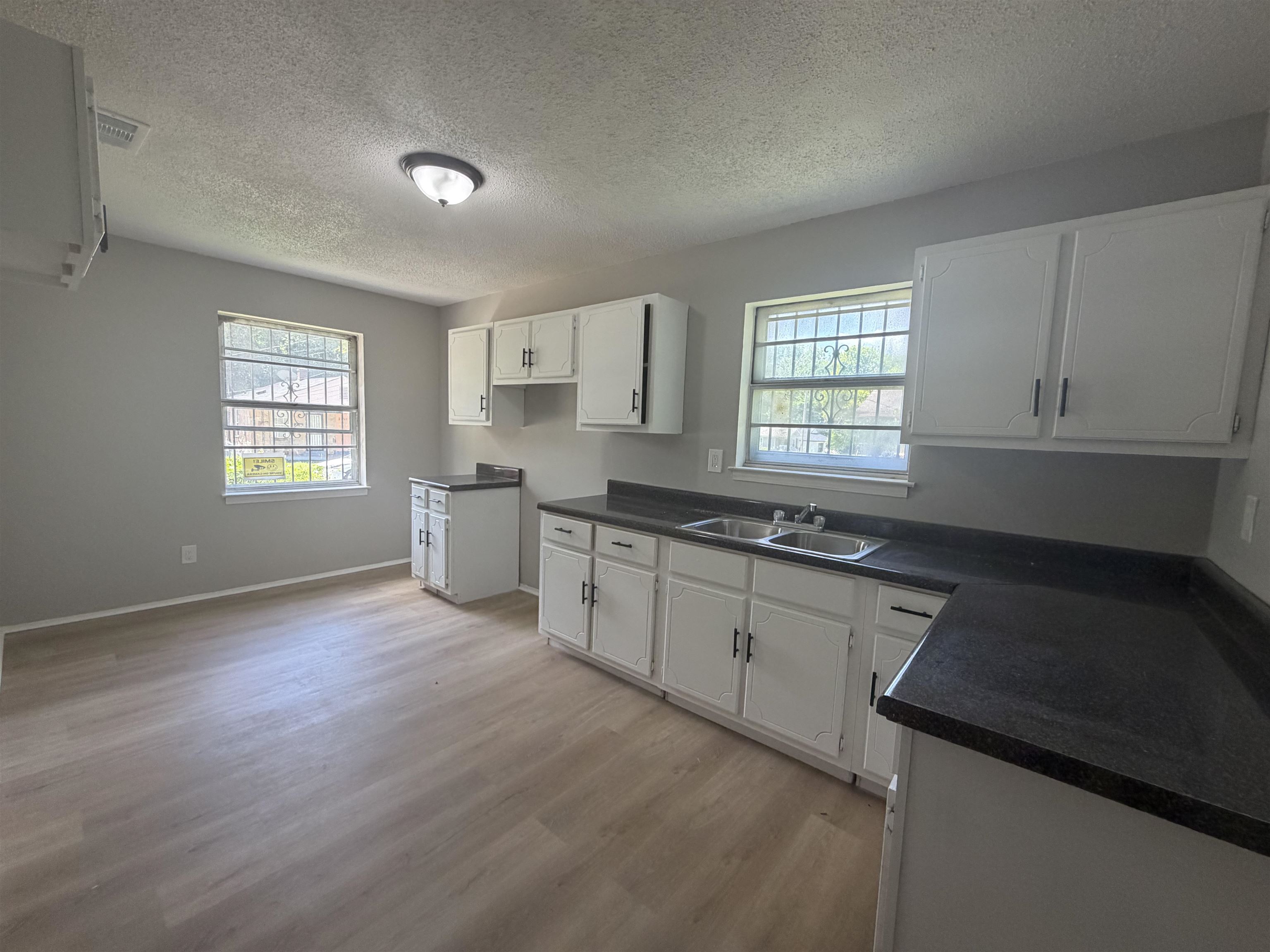 2402 Shasta Avenue Memphis, TN 38108 - Photo 6 of 7 Bright kitchen featuring light wood-finish flooring, white cabinetry with dark hardware, dark countertops, and a dual basin stainless steel sink