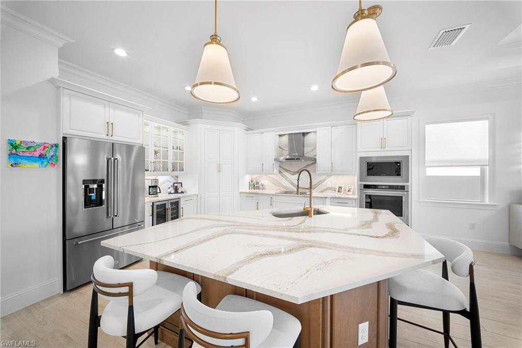8923 Gustavia Court Naples, FL 34113 - Photo 18 of 50 a kitchen with stainless steel appliances kitchen island a table chairs sink and microwave