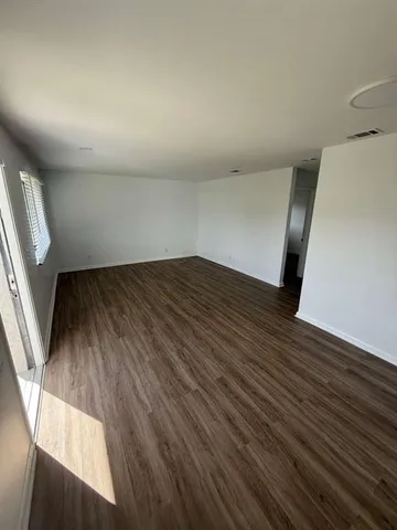 a view of an empty room with wooden floor and a window