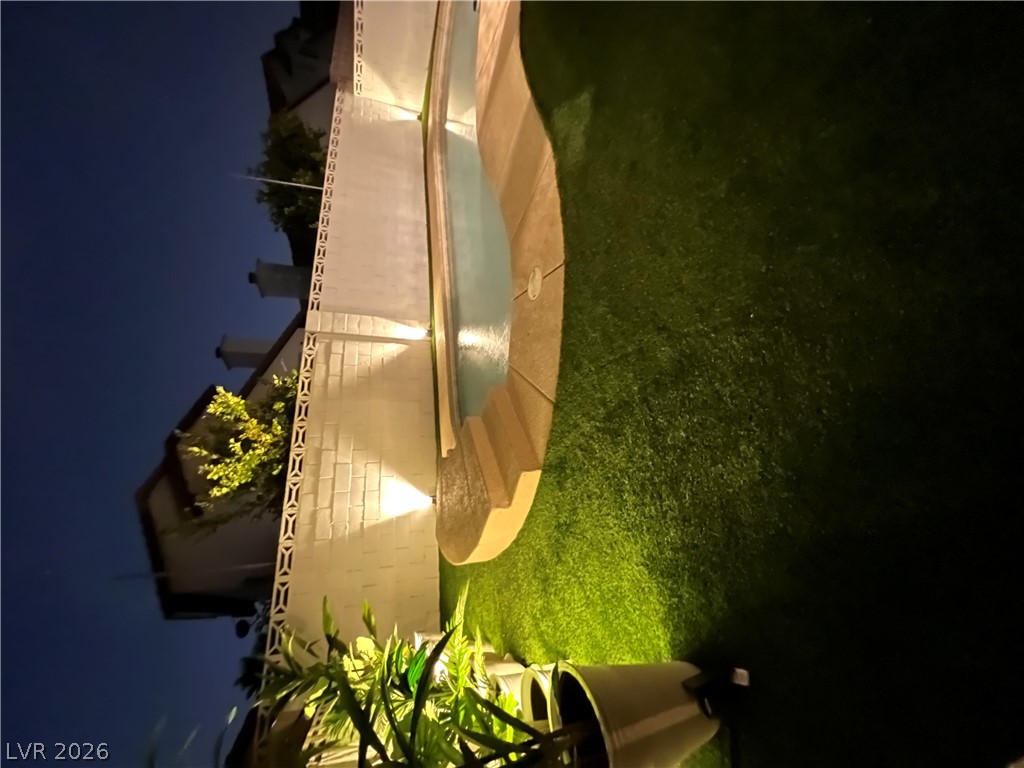 6505 Deadwood Road Las Vegas, NV 89108 - Photo 31 of 33 An illuminated lawn surrounds a captivating pool, offering tranquil evening enjoyment.