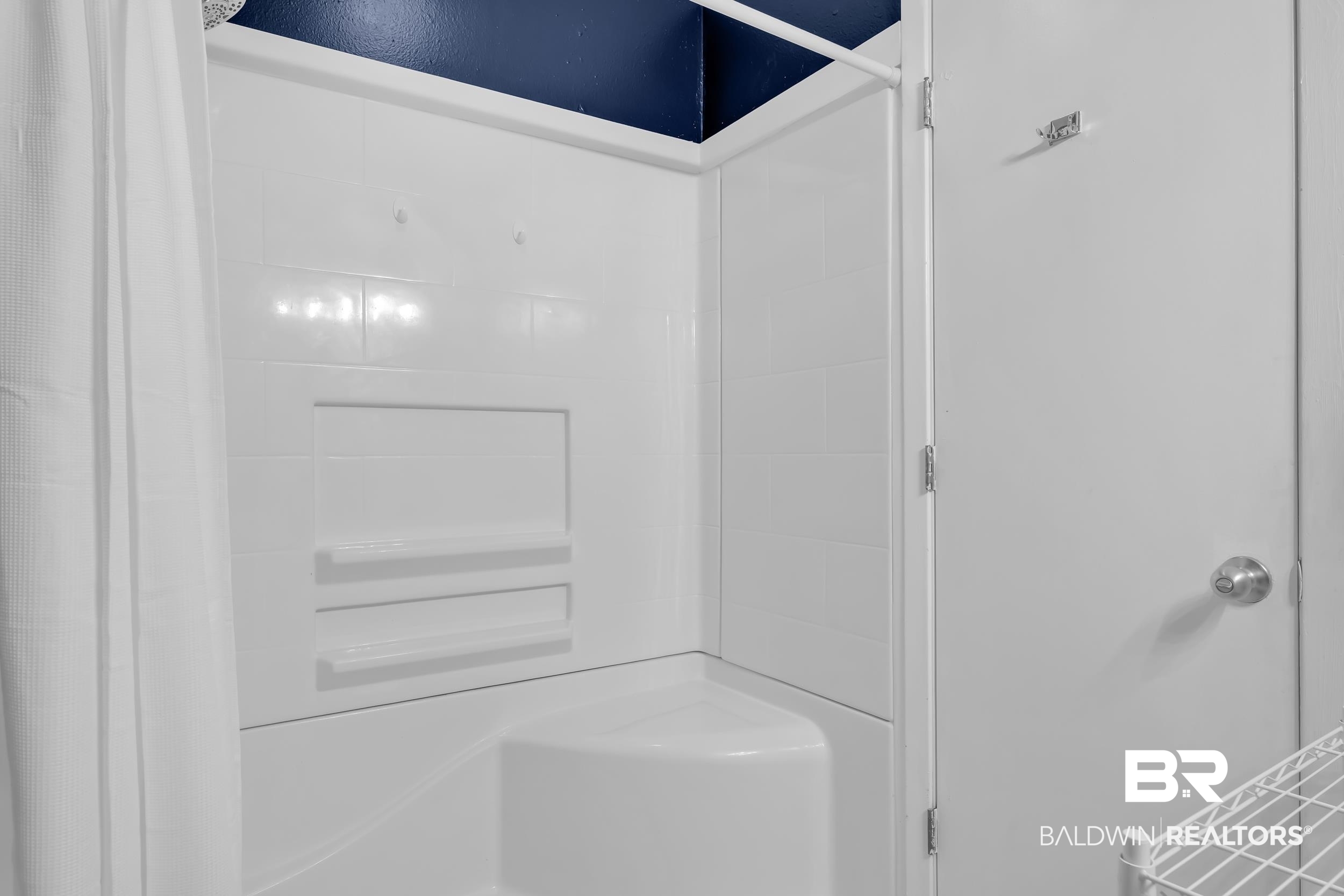 27222 Gulf Road, Unit 33 Orange Beach, AL 36561 - Photo 16 of 29 White shower enclosure featuring an integrated corner seat, two recessed shelves, and white surround walls