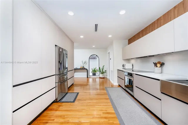 a large white kitchen with stainless steel appliances granite countertop a stove a refrigerator and a sink with wooden floor