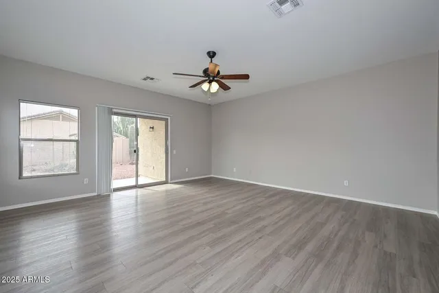 an empty room with wooden floor chandelier fan and windows