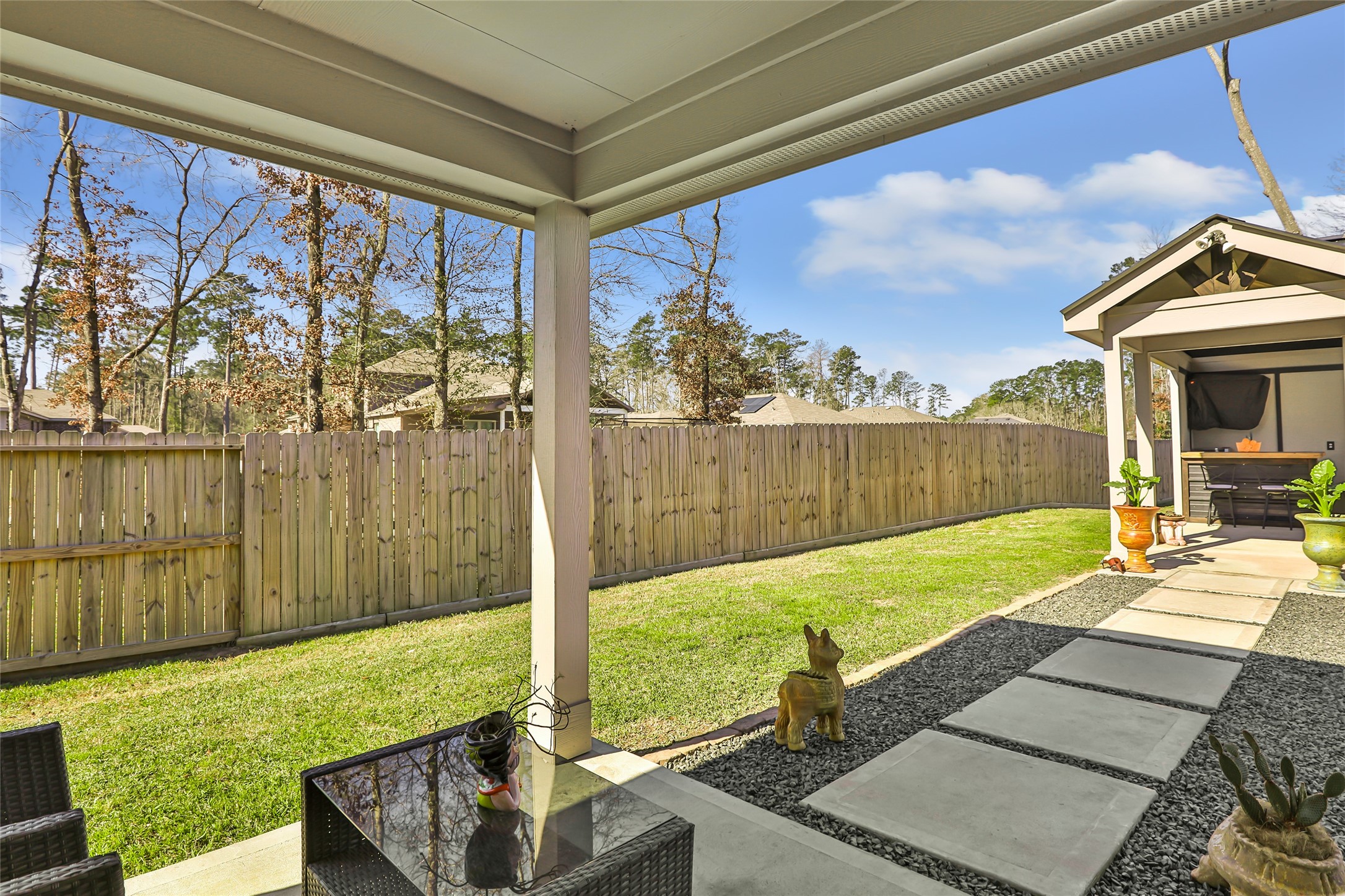 811 Republic Road New Caney, TX 77357 - Photo 5 of 37 This photo showcases a spacious backyard with a covered patio area, neatly landscaped lawn, and a wooden privacy fence. The seating area and pathway enhance the outdoor living space, perfect for relaxation and entertainment.