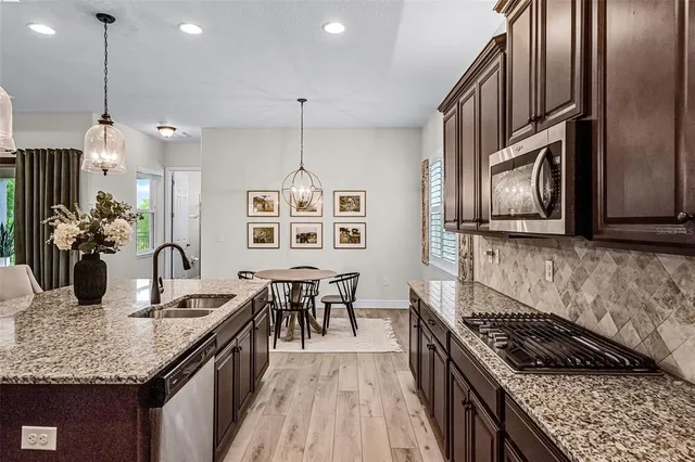 a kitchen with granite countertop a stove a sink dishwasher a refrigerator and a dining table with wooden floor