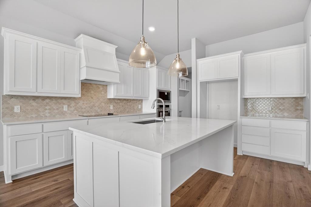 504 Clifton Court Springtown, TX 76082 - Photo 12 of 36 Kitchen featuring a large central island with a sink, white cabinetry, integrated stainless steel appliances, and wood-finish flooring