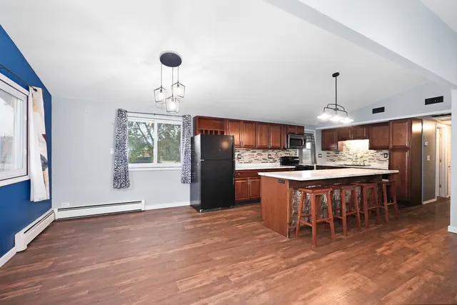 a kitchen with stainless steel appliances granite countertop a refrigerator a sink dishwasher a dining table and chairs with wooden floor